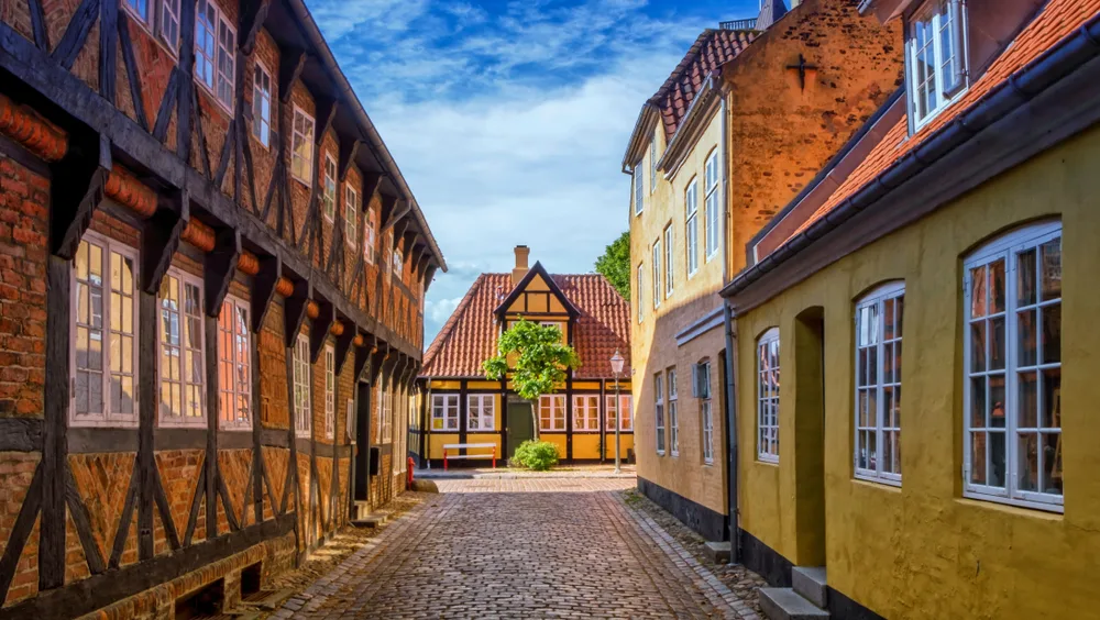 Cozy and quaint yellow homes in Ribe, Denmark, pictured in the summer, the best time to visit, with blue skies overhead