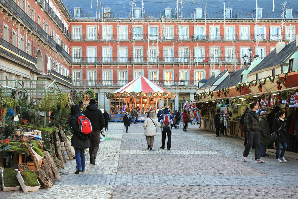 Few people walking around a paved road surrounded by stately and industrial looking red-brick buildings in Madrid during the winter, the least busy time to visit
