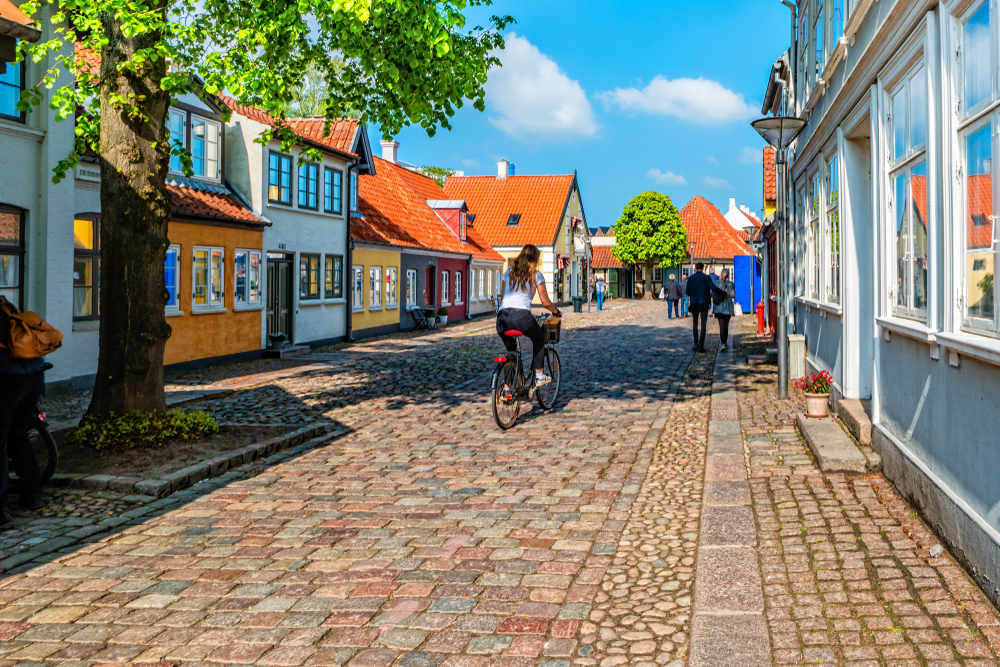 Colorful homes pictured during the best time to visit Denmark, the summer, in Odense with people riding their bikes along the cobblestone street
