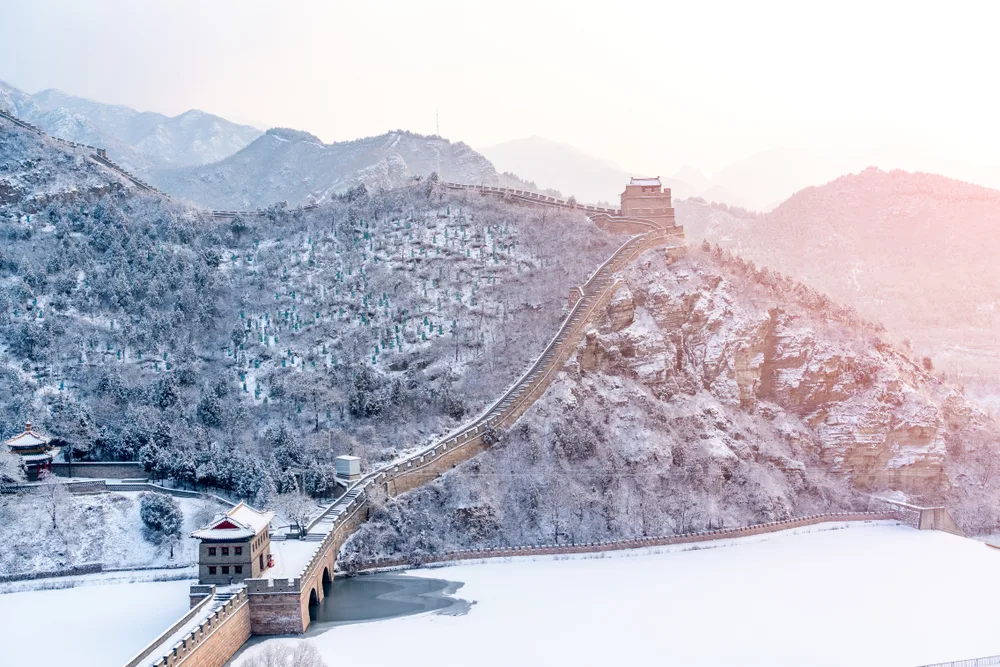 Aerial view of the Great Wall pictured with snow on it and on the ground around it in the winter, which is the overall cheapest time to visit China
