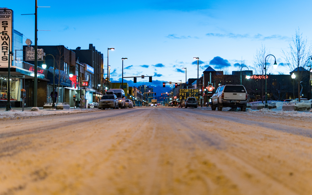 Pictured during the least busy time to visit, snow on the ground in Anchorage in a city with a close-up of the road pictured at dusk