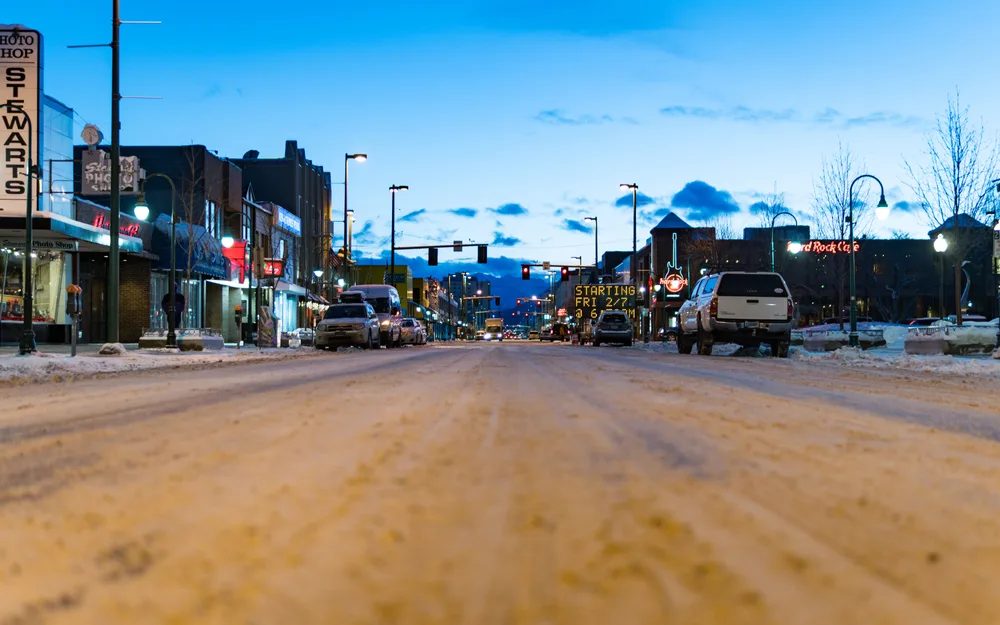 Pictured during the least busy time to visit, snow on the ground in Anchorage in a city with a close-up of the road pictured at dusk