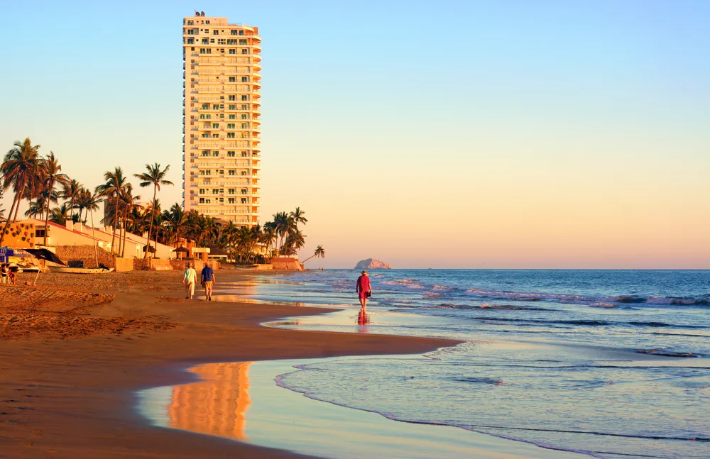 People in pants bundled up and walking on the empty beaches of Mazatlan during the winter, the worst time to visit
