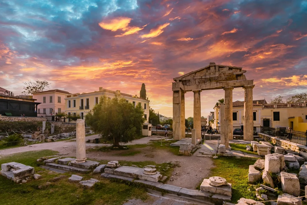 Ancient Roman forum ruins below a purple and yellow dusk sky pictured during the best time to travel to Athens, the spring