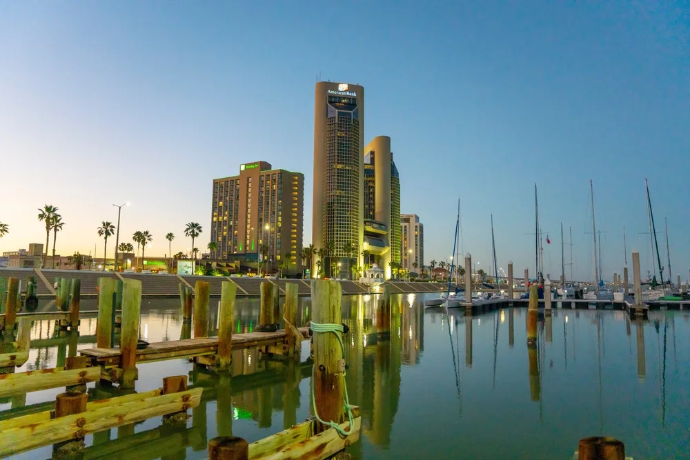 Bayfront downtown area pictured during the overall best time to visit Corpus Christi with its three tall modern buildings towering over the water and boats below