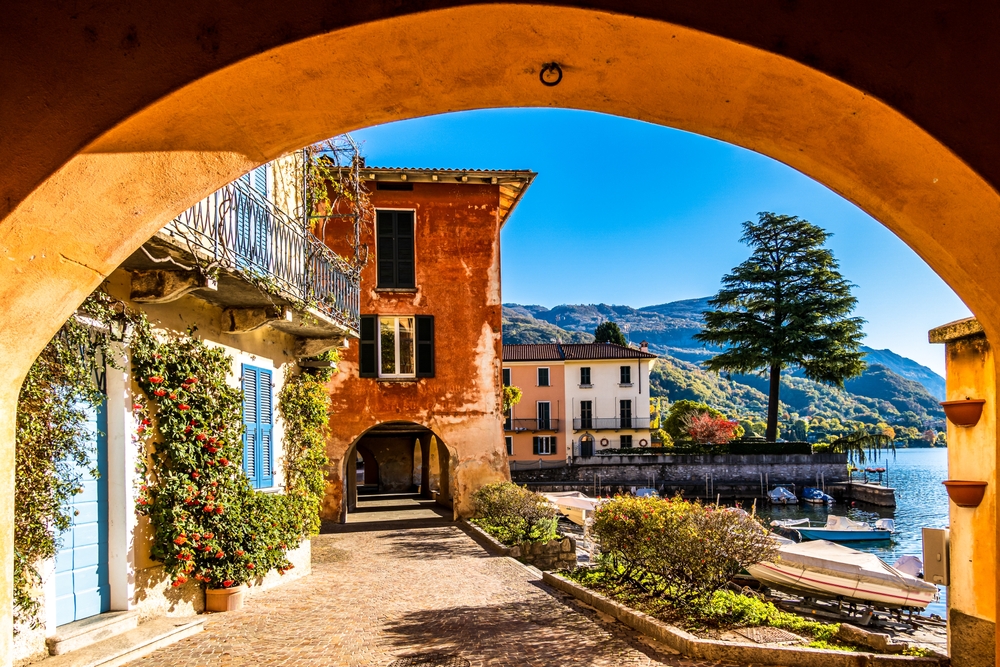 Old town of Mandello seen from under the arches during the least busy time to visit Lake Como with blue skies peaking out from behind the orange buildings
