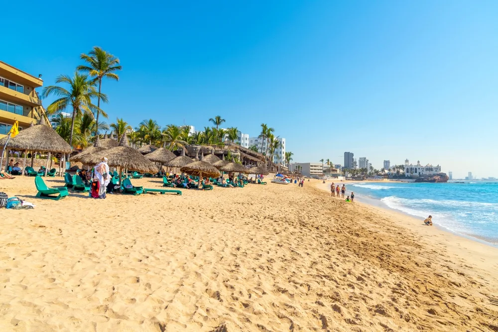 Golden Zone beach with beige beaches and teal water with people lying on the beach and playing in the water below deep blue skies for a piece on the best time to visit Mazatlan
