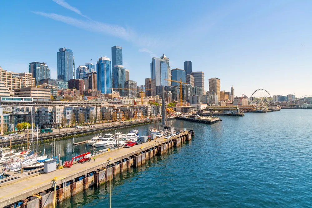Photo of the Great Wheel and Puget Sound pictured next to the pier with the downtown skyline towering over the water for a guide titled best time to visit Seattle