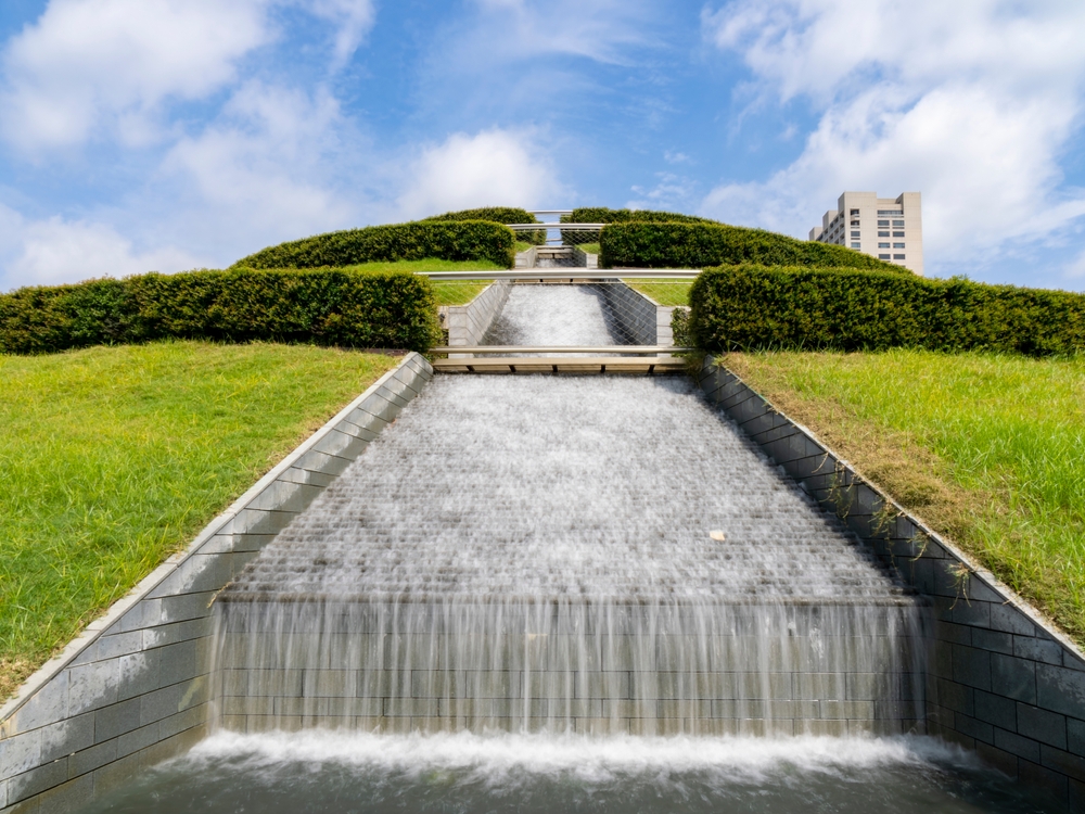 Waterfall cascading down from the hilltop in McGovern Gardens, pictured during the best time to visit Houston, with shrubs and hedges lining the various tiers of the hill