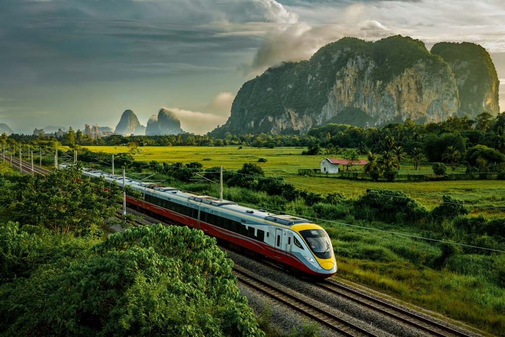 Amazing postcard view of a yellow and red train making its way down the tracks next to rice fields with huge towering cliffs on either side of the tracks