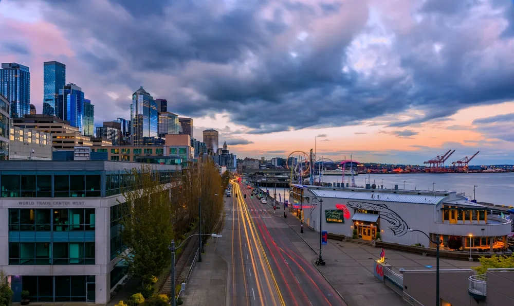 Gorgeous view of a long exposure image of Seattle's waterfront with cars driving by and cloudy skies overhead, seen at dusk