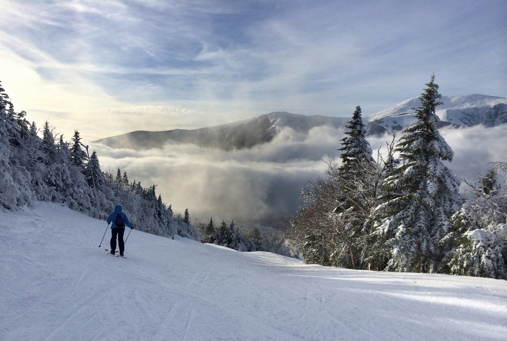 Ski resort in New Hampshire pictured during the month's least busy time to visit, the winter, pictured with a hazy mountain and valley below in front of a guy skiing
