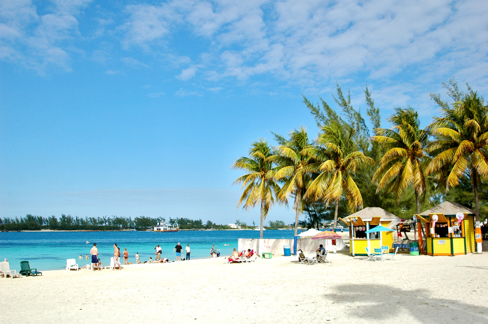 Photo of a semi-crowded city beach during the best time to visit Nassau with lovely white sand and vibrant green trees below blue sky
