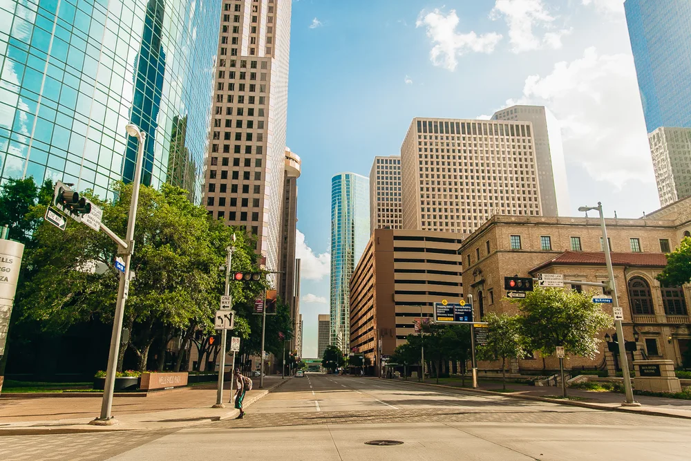 Empty streets pictured on a clear summer day with a lone man walking across a street under tall buildings for a guide to the best and worst times to visit Houston