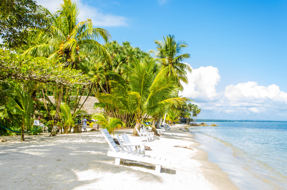 Photo of the gorgeous white sand beach in Livingston, Guatemala, pictured with a few white loungers on the otherwise empty and tree-lined beach, seen during the best time to visit Guatemala