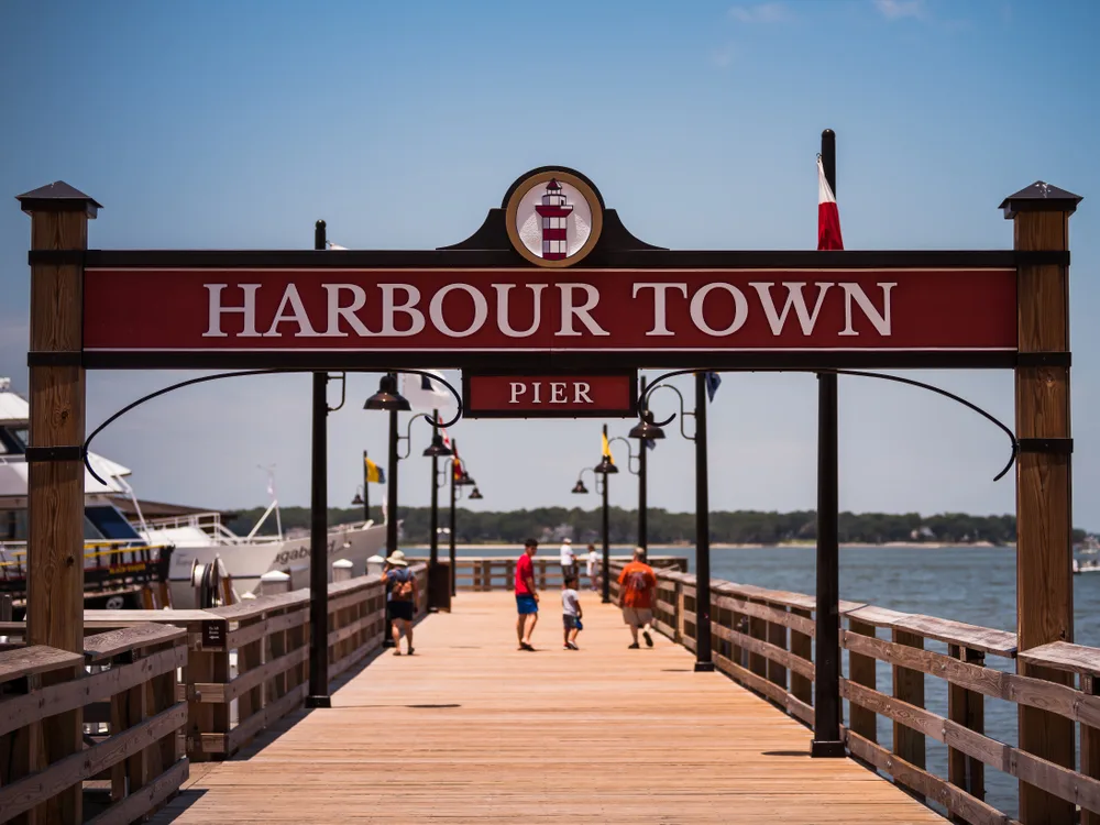 Harbour Town pier next to boats with a few families walking along it pictured during the best time to visit Hilton Head
