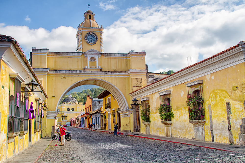 Photo of the old stone streets in the middle of Antigua pictured with clouds overhead and yellow walls all around, during the overall best time to visit Guatemala