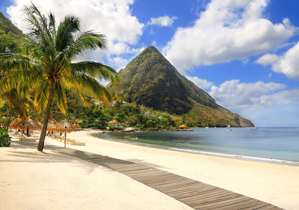Gorgeous white sand beach in Saint Lucia pictured under blue skies with a large volcano in the background