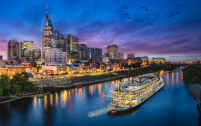 Featured image for a piece titled Is Nashville Safe to Visit featuring a dark night sky over the river and a boat making its way down the water canal
