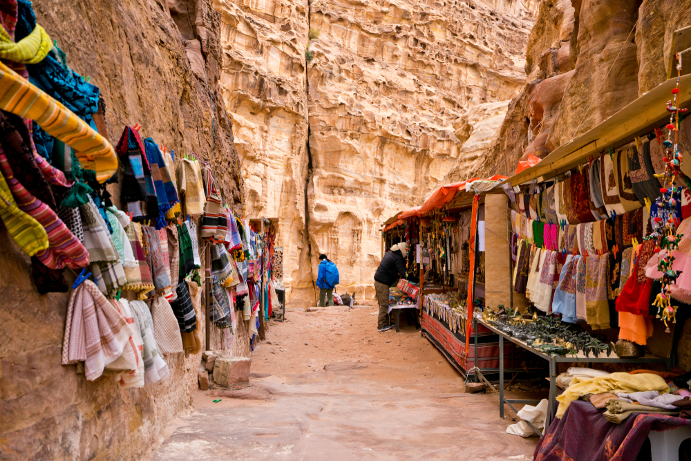 To help answer "is Jordan safe to visit," a market in Petra with colorful rugs hanging from wooden display racks