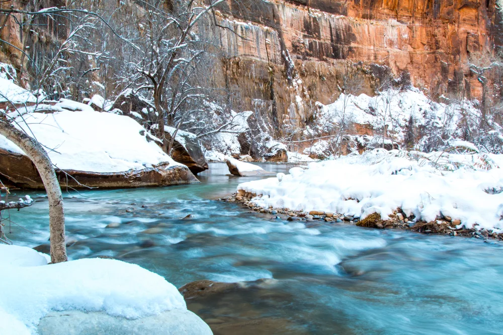 Winter in the canyon pictured during the least busy time to visit Zion National Park with a cold river running through snow-capped valleys