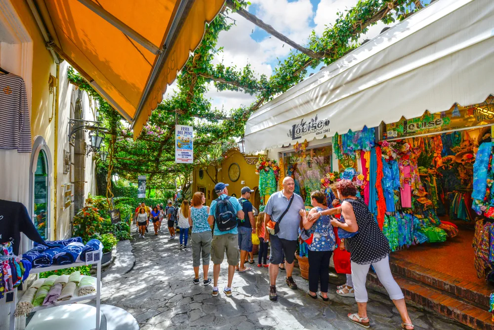 People walking in an open-air market in Positano during the town's best time to visit under umbrella shades