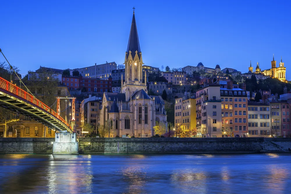 Night view of a purple sky over the church and town-lined river during the overall best time to visit Lyon, France