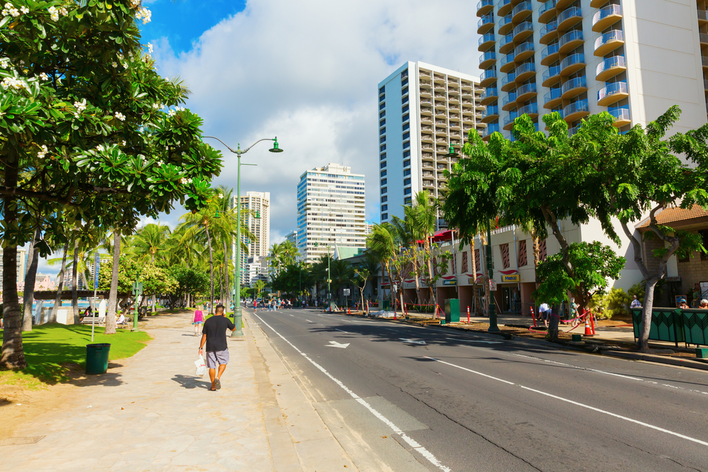 Photo of a man walking down the sidewalk in Honolulu between big and tall condo buildings