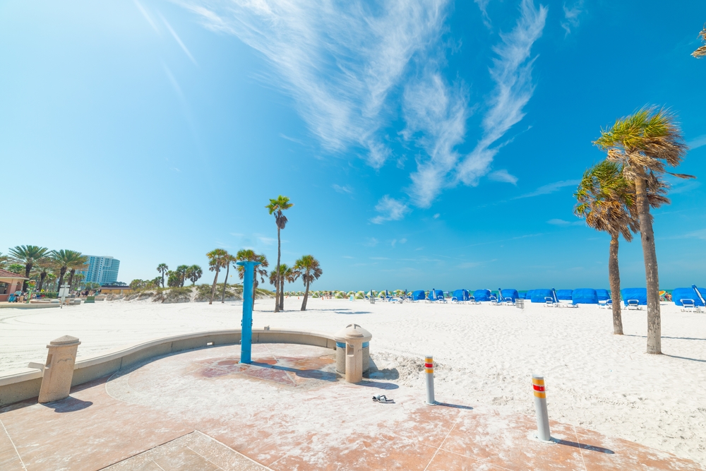 Entrance to an empty beach pictured during the best time to visit Clearwater, FL with white sand and dark blue skies above