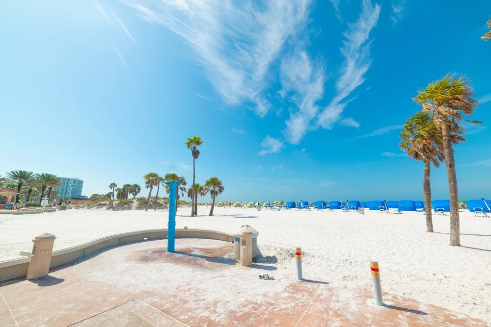 Entrance to an empty beach pictured during the best time to visit Clearwater, FL with white sand and dark blue skies above