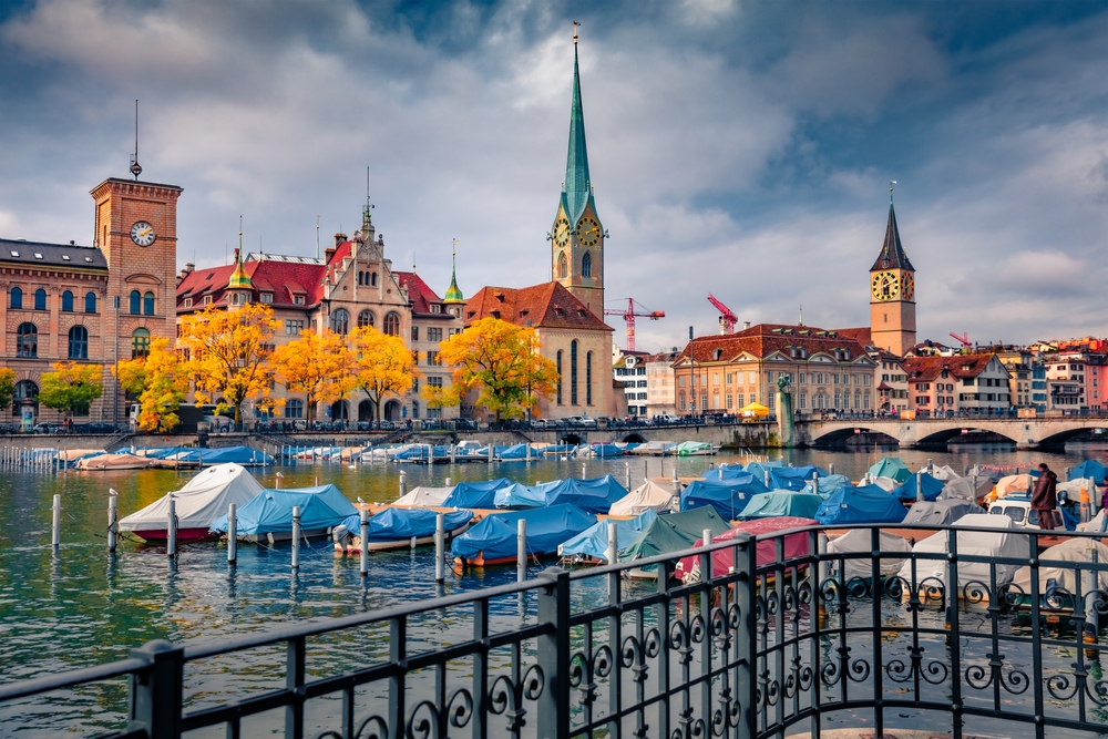 Wonderful mid-autumn day with fall foliage on the trees pictured under a gloomy sky with covered boats on stands in the lake during the fall, the cheapest time to visit Zurich