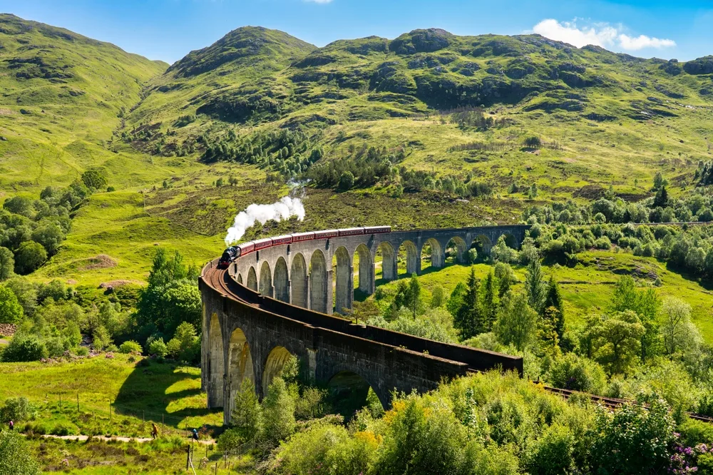 Pictured during the spring, the overall best time to visit the UK, the Glenfinnan Railway train makes its way over the viaduct and is surrounded by lush green vegetation