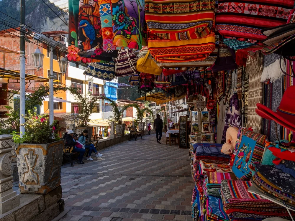 Pictured during the overall cheapest time to visit Machu Picchu, a market in Aguas Calientes (a town at the base of the mountain) is seen with rugs on the side of the photo and few people around