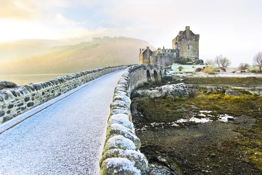 Pictured during the least busy time to visit the UK, winter , the Eilean Donan Castle is pictured with snow all around and an orange sky behind it