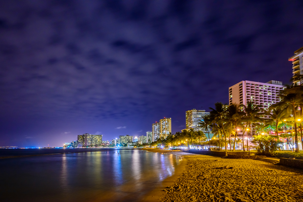Night view of Waikiki Beach pictured under a dark night sky with hotels lining the beach for a guide to whether or not Hawaii is safe to visit