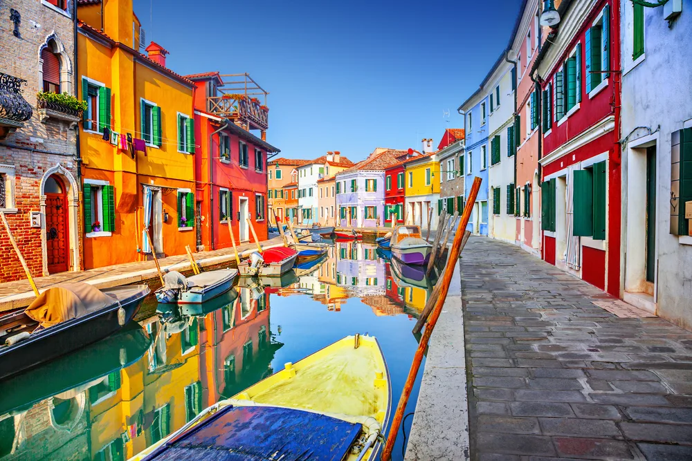 Colorful houses next to boats on still water pictured during the overall best time to visit Venice, the spring