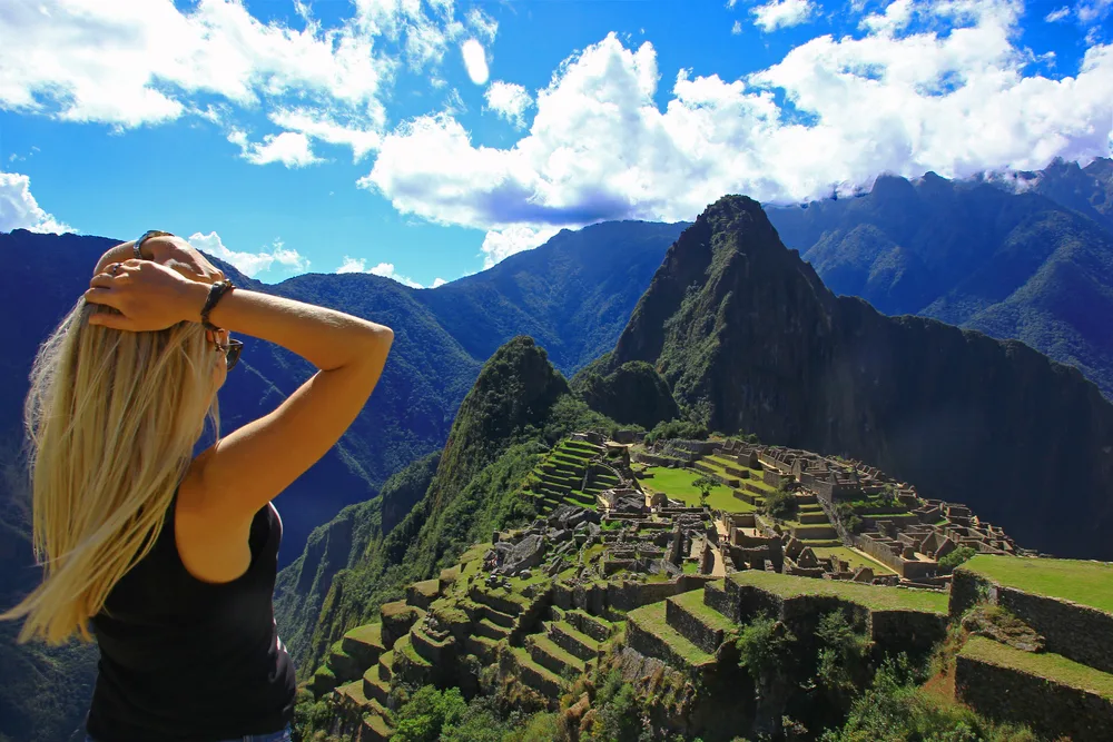 Woman in a blue shirt holding her head during the best time to visit Machu Picchu, with a blue sky above the mountain