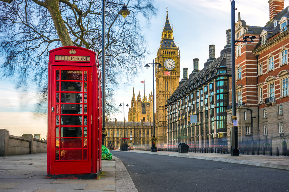 Neat view of a red phone booth outside of Big Ben pictured during the best time to visit the UK, with clear blue skies and few people on the streets