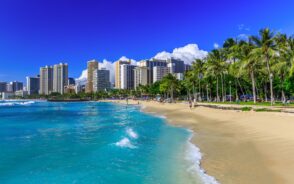 Photo of the beige sand on Waikiki Beach pictured under blue sky during the overall best time to visit Oahu, the summer