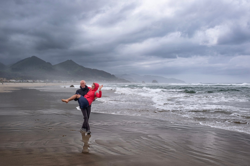 Man holding his wife on a rainy day on Cannon Beach during the worst time to visit
