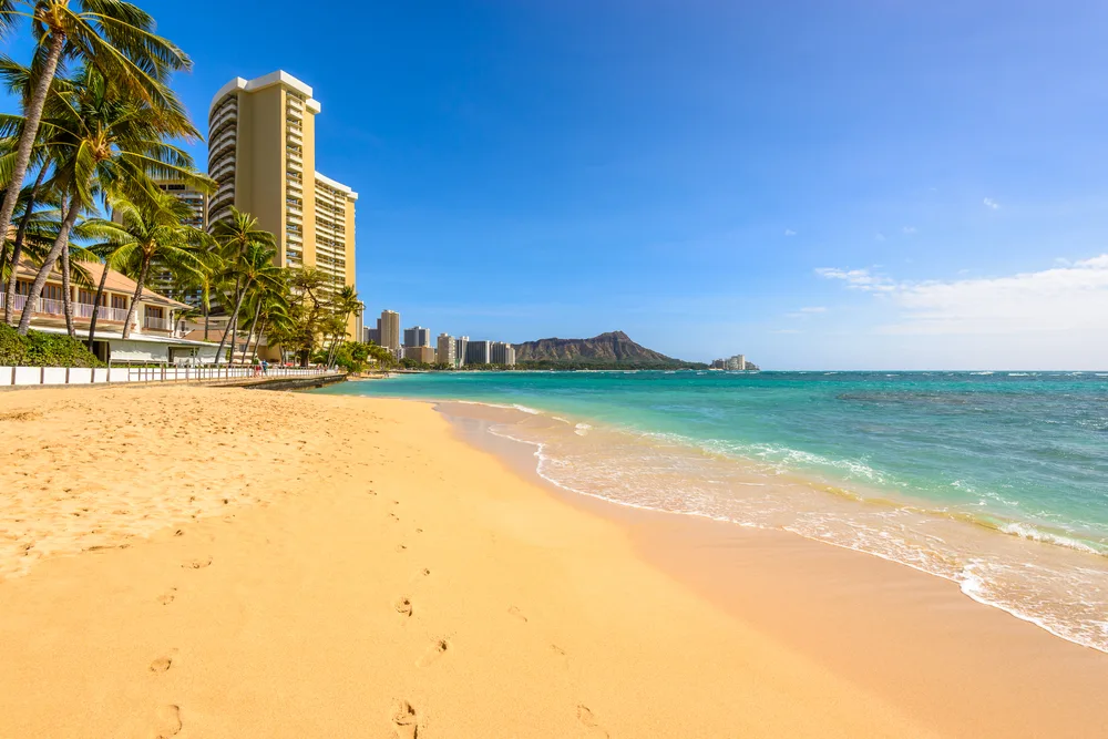 Neat view of the tan sand outside of a resort area under blue sky during the overall best time to visit Oahu, the spring