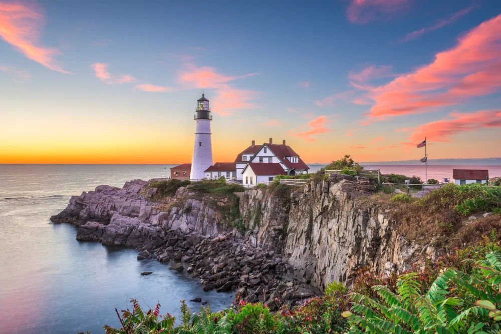 Lighthouse in Portland Maine pictured under a nice calm dusk sky with calm seas gently lapping a rocky coastline pictured during the best time to visit New England