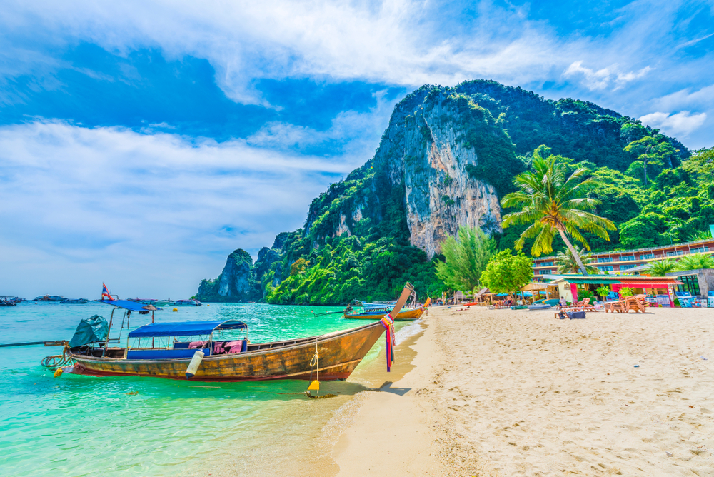 Pictured during the low season, a single boat floats on an otherwise empty bay with nobody on the beach and clouds high overhead during the cheapest time to visit Thailand
