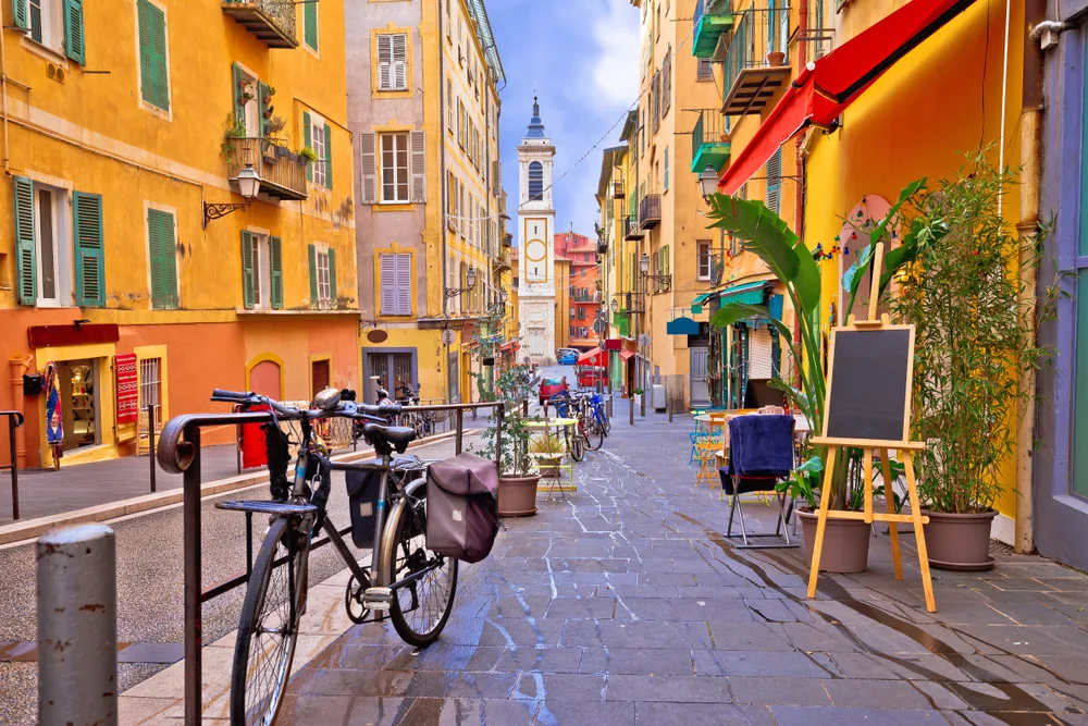 Pictured during the cheapest time to visit France, a street with yellow and orange buildings on either side with a bike on the stone path