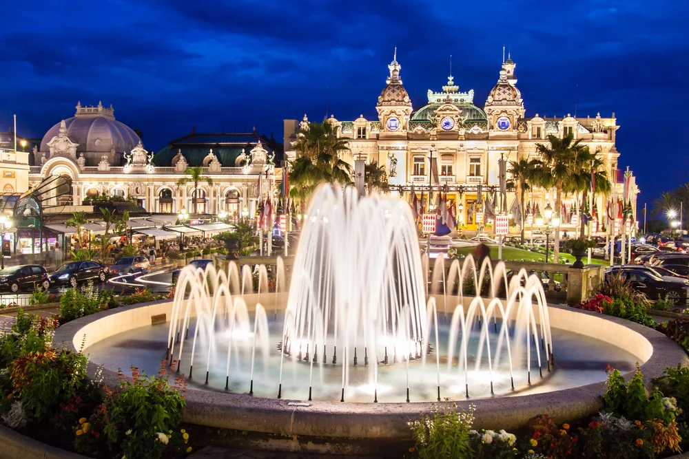 View of the Monte-Carlo Casino outdoor fountain at night with the illuminated architecture around it creating a beautiful scene for a frequently asked questions section on the best months to visit Monaco