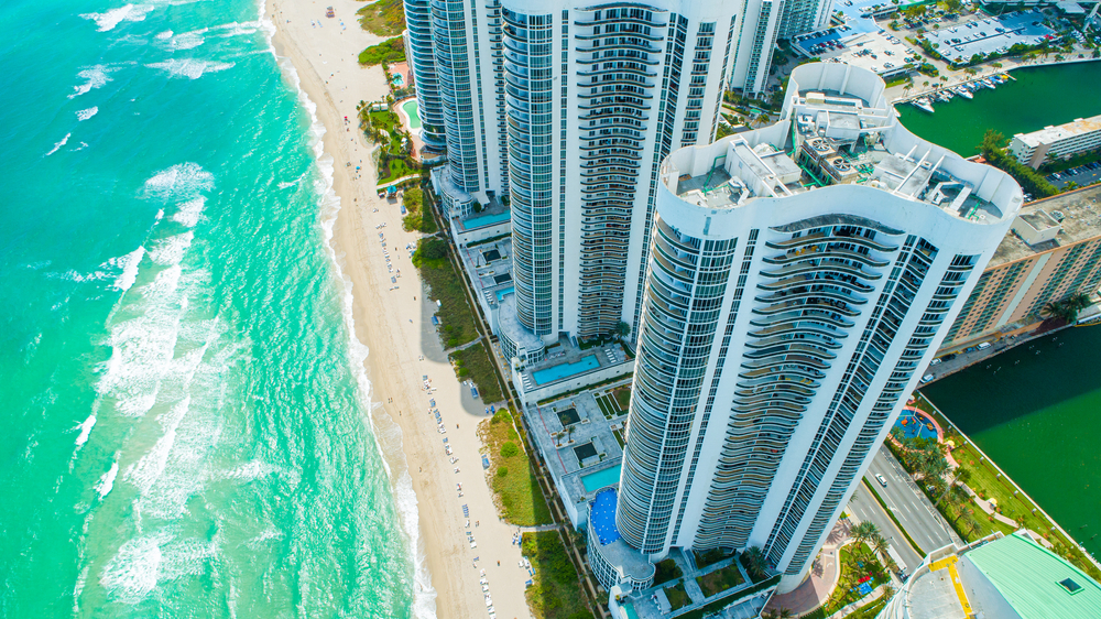Aerial view of Sunny Isles Beach, great for snorkeling, during the overall best time to visit Miami in Florida with turquoise water and white sand as high-rises stand behind the beach