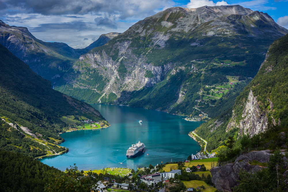 Geiranger Fjord seen from above with a lone boat on the water and blue skies overhead for a section describing the worst time to visit Norway