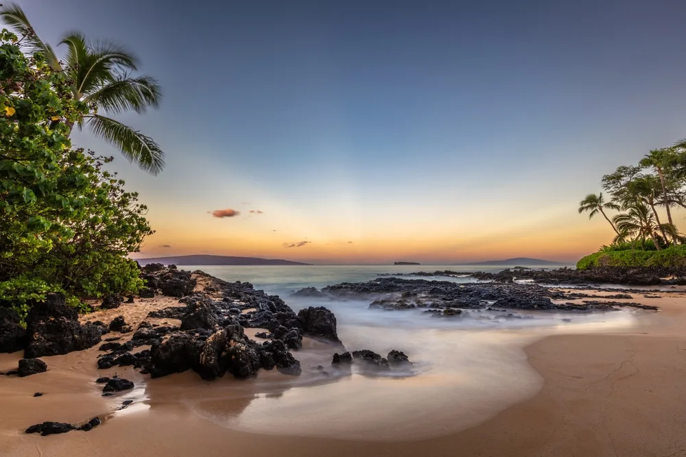 Pa'ako Cove in South Maui seen at sunset with rocks and palm trees on the golden sand for a frequently asked questions section giving information on the best time to visit Hawaii 