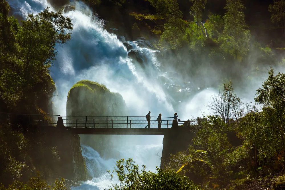 Waterfall seen near Briksdal Glacier in Norway with people crossing the bridge amid mist and fog during the least busy time to visit Norway