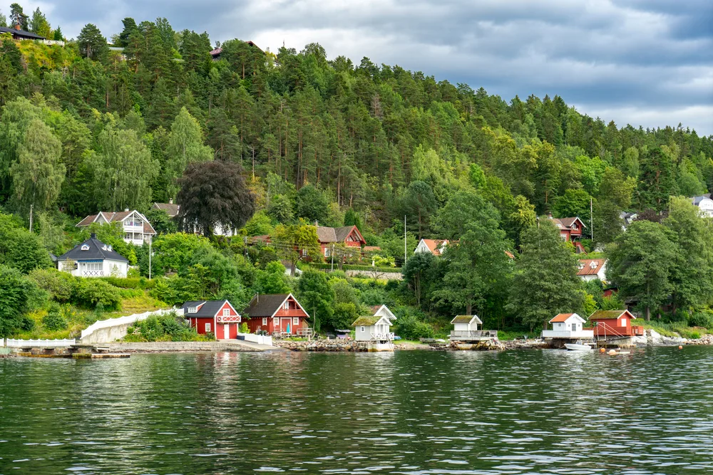 Small, colorful homes on the edge of the Oslofjord just outside the capital with green trees surrounding them during the best time to visit Norway